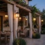 Pergola adosada de madera envejecida con cerramientos textiles tecnicos mobiliario de ratan y sistema de iluminacion de estilo colonial