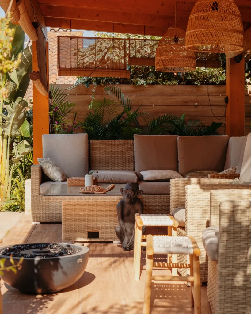 Cenador tropical con muebles de ratán sintético, lámparas de mimbre acampanadas, cortinas de bambú y fogatero de piedra. Cenador tropical con muebles de ratan sintetico lamparas de mimbre acampanadas cortinas de bambu y fogatero de piedra